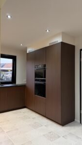 Gewrapte keuken in Edegem met een hoge kastenwand in een warme donkere houtlook