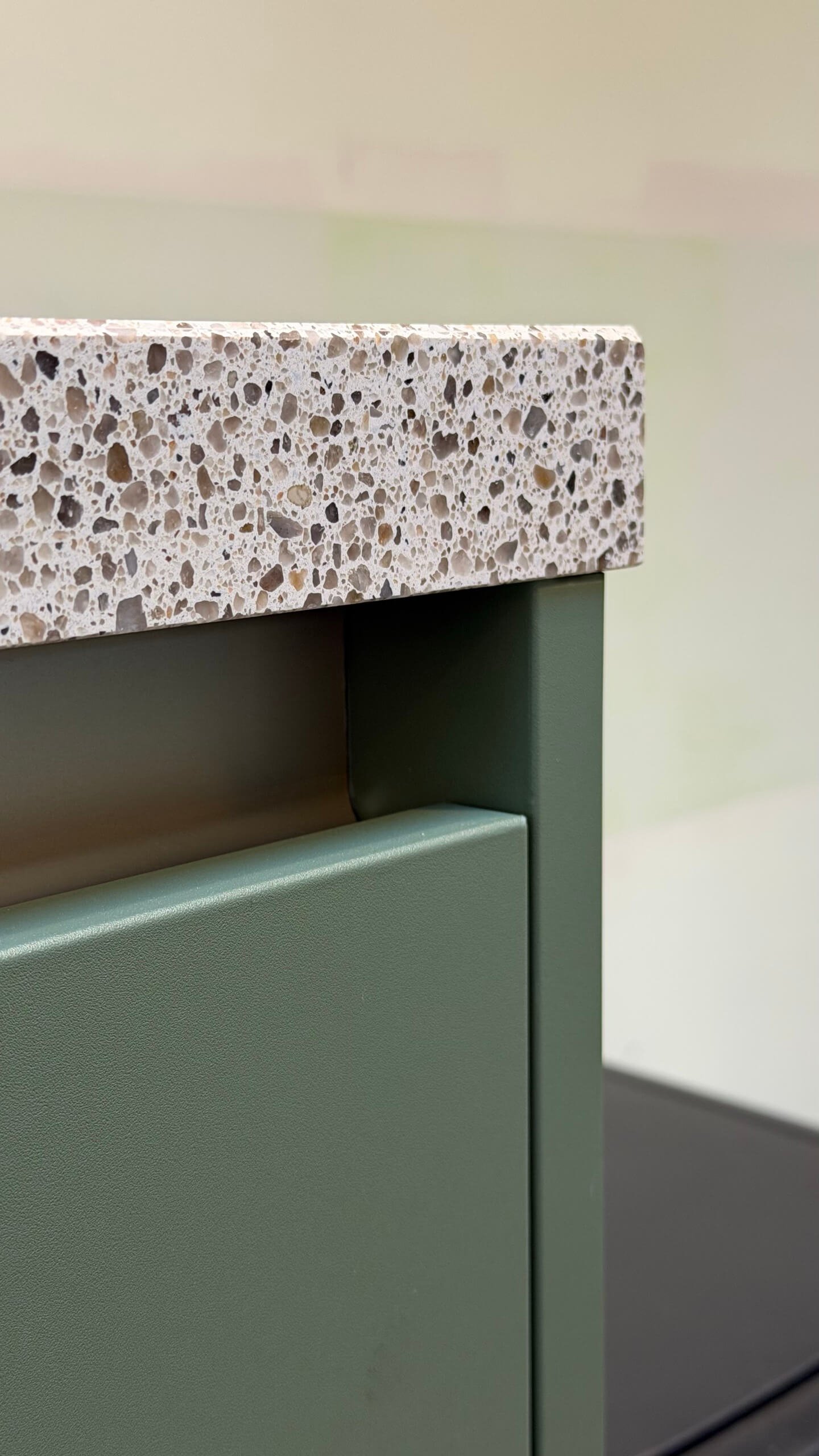 Close-up van de strakke randafwerking van een groen gewrapt keukenfront naast het terrazzo werkblad