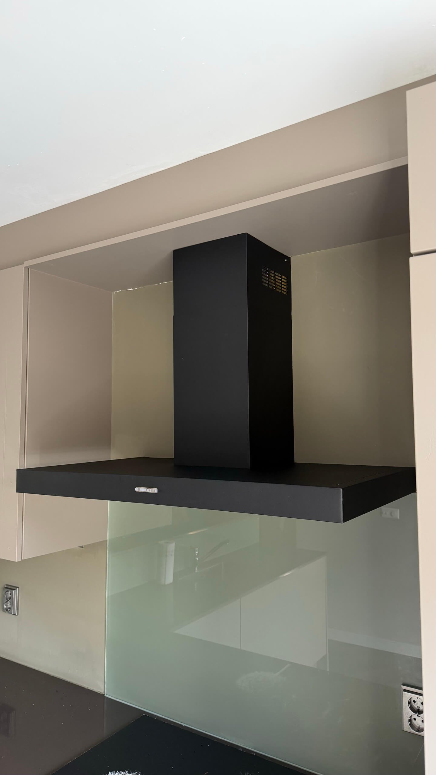 Zwarte afzuigkap in Pure black boven het kookvlak, met taupe kastjes eromheen