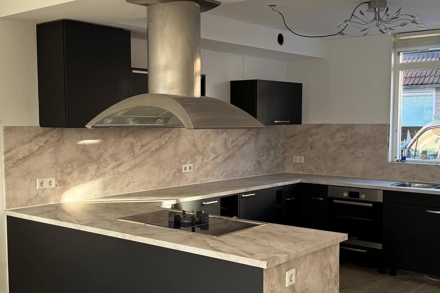 Gewrapte keuken in Pure black met een werkblad en achterwand in de marmerlook Onyx gold