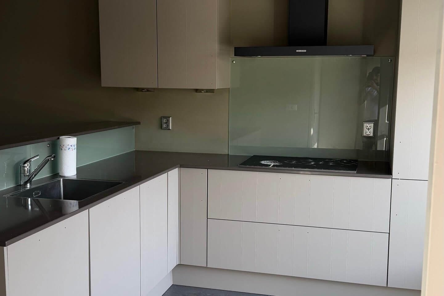 Gewrapte keuken in de taupetint Mesa met een zwarte afzuigkap en een groene glazen achterwand