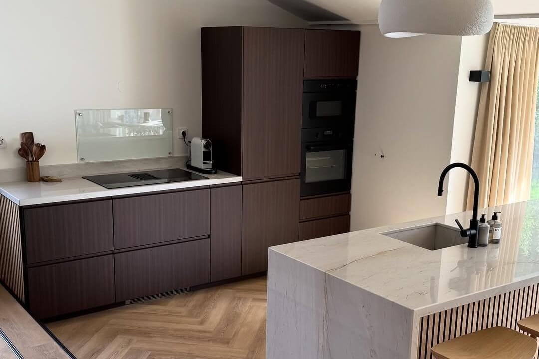 Gewrapte keuken met donkere fronten en een licht kookeiland in marmerlook
