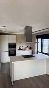 Gewrapte keuken in Rotterdam met kasten en kookeiland in de lichte beton cire look Fractura shell 2.0 en werkbladen in de crème marmerlook Crema