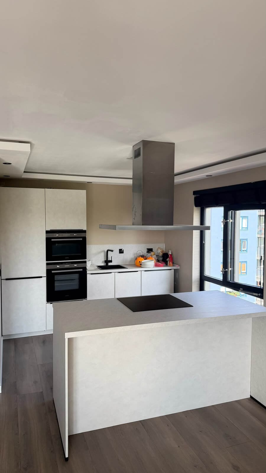 Gewrapte keuken in Rotterdam met kasten en kookeiland in de lichte beton cire look Fractura shell 2.0 en werkbladen in de crème marmerlook Crema