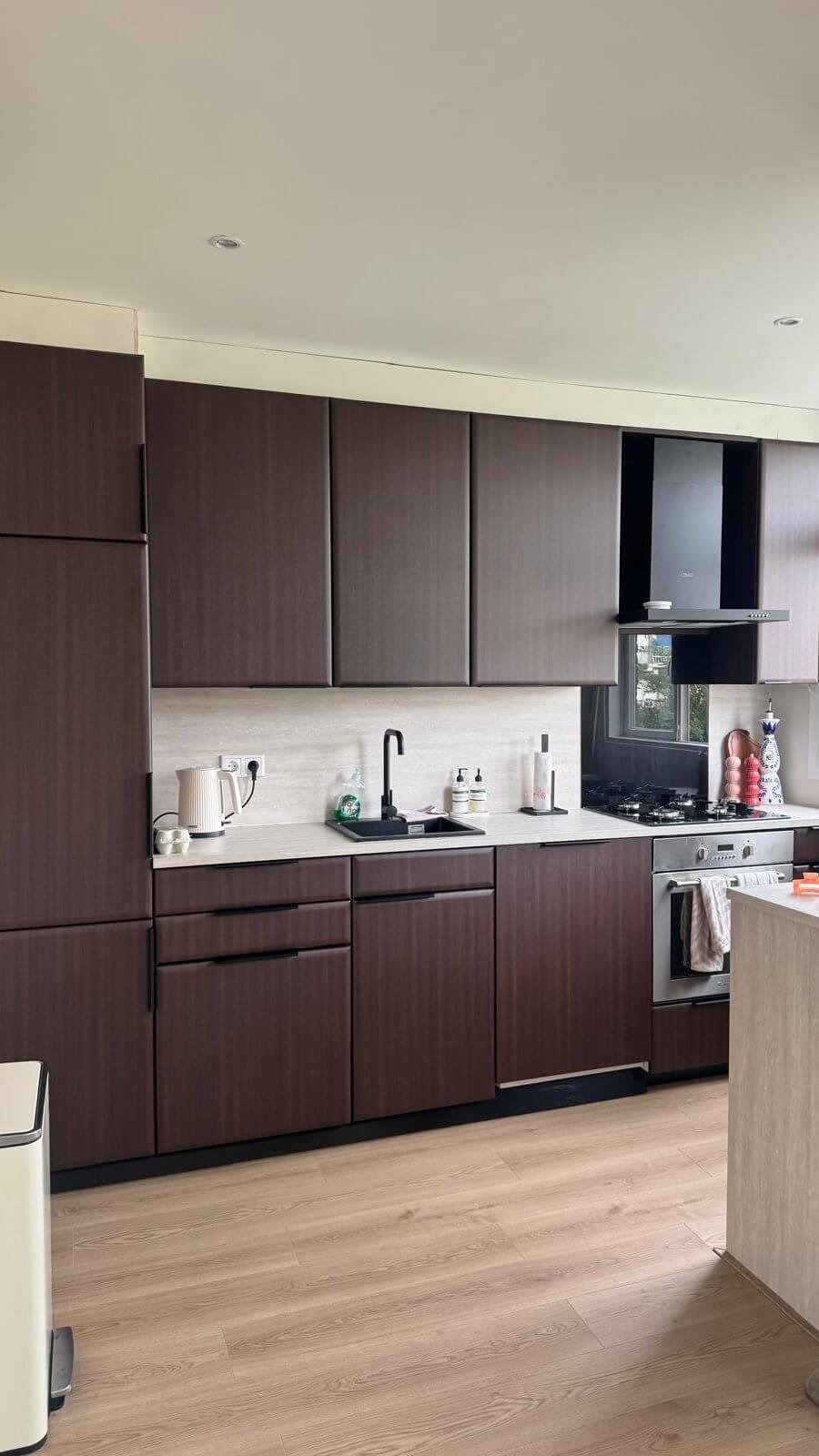 Gewrapte keuken in Schiedam met kasten in de warme donkere houtlook Chestnut, een lichte achterwand en een licht werkblad