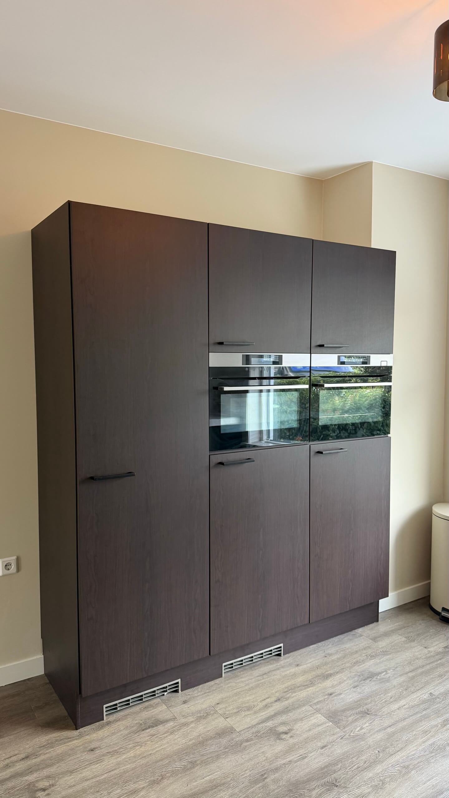 Hoge kastenwand met ingebouwde ovens, gewrapt in de donkere houtlook Navis